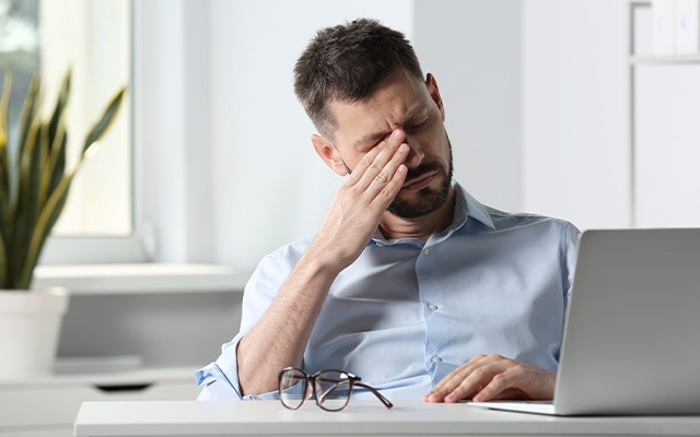 Mann mit trockenen Augen sitzt am Schreibtisch